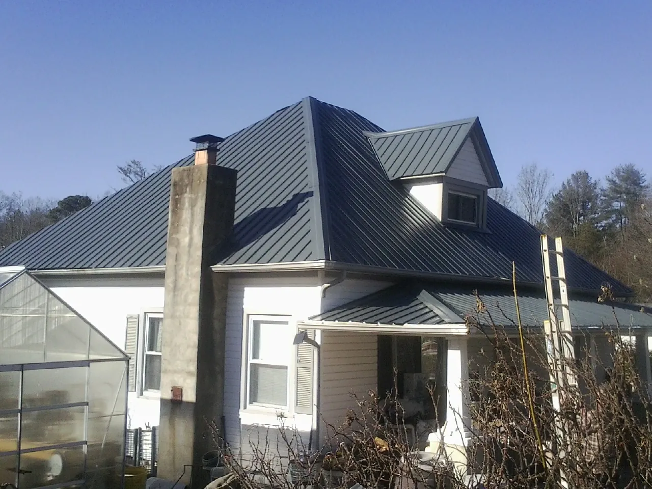 Dark blue standing seam metal roof on a white farmhouse with dormer — Slate & Tile Roof Repair by Roofing Brothers in Century