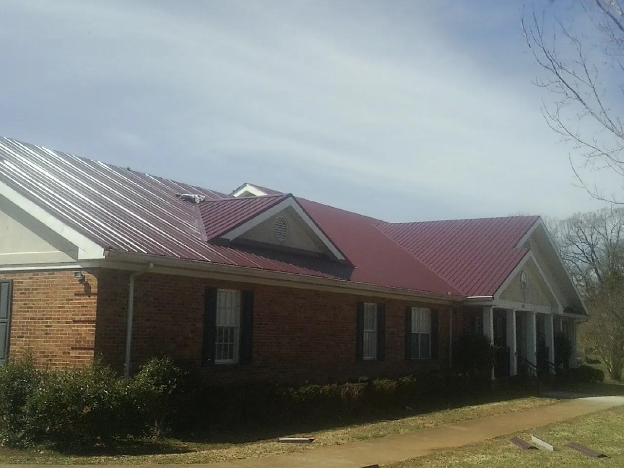 Red metal roof with gabled entries on a long brick building, from a Hail Damage Roof Repair job in Century