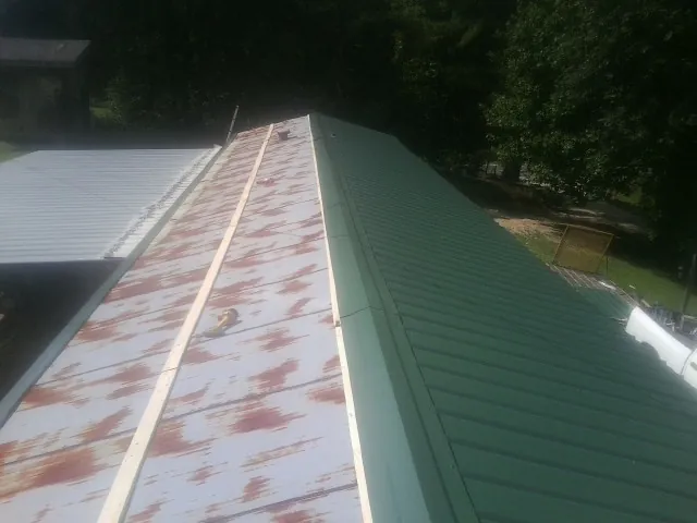 Old rusted panels beside newly installed green metal roofing — Wind Damage Roof Repair by Roofing Brothers in Century