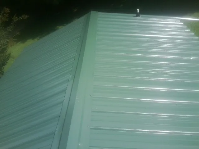 New green metal panels meeting at the ridge of a roof — Flat Roof Repair work by our crew in Century