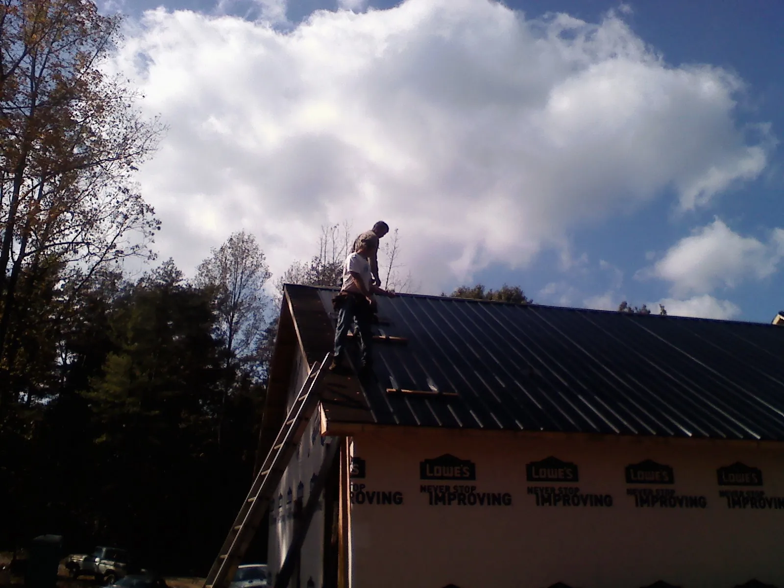 Roofer fastening dark metal panels high against a cloudy sky, from a Roof Inspection job in Century