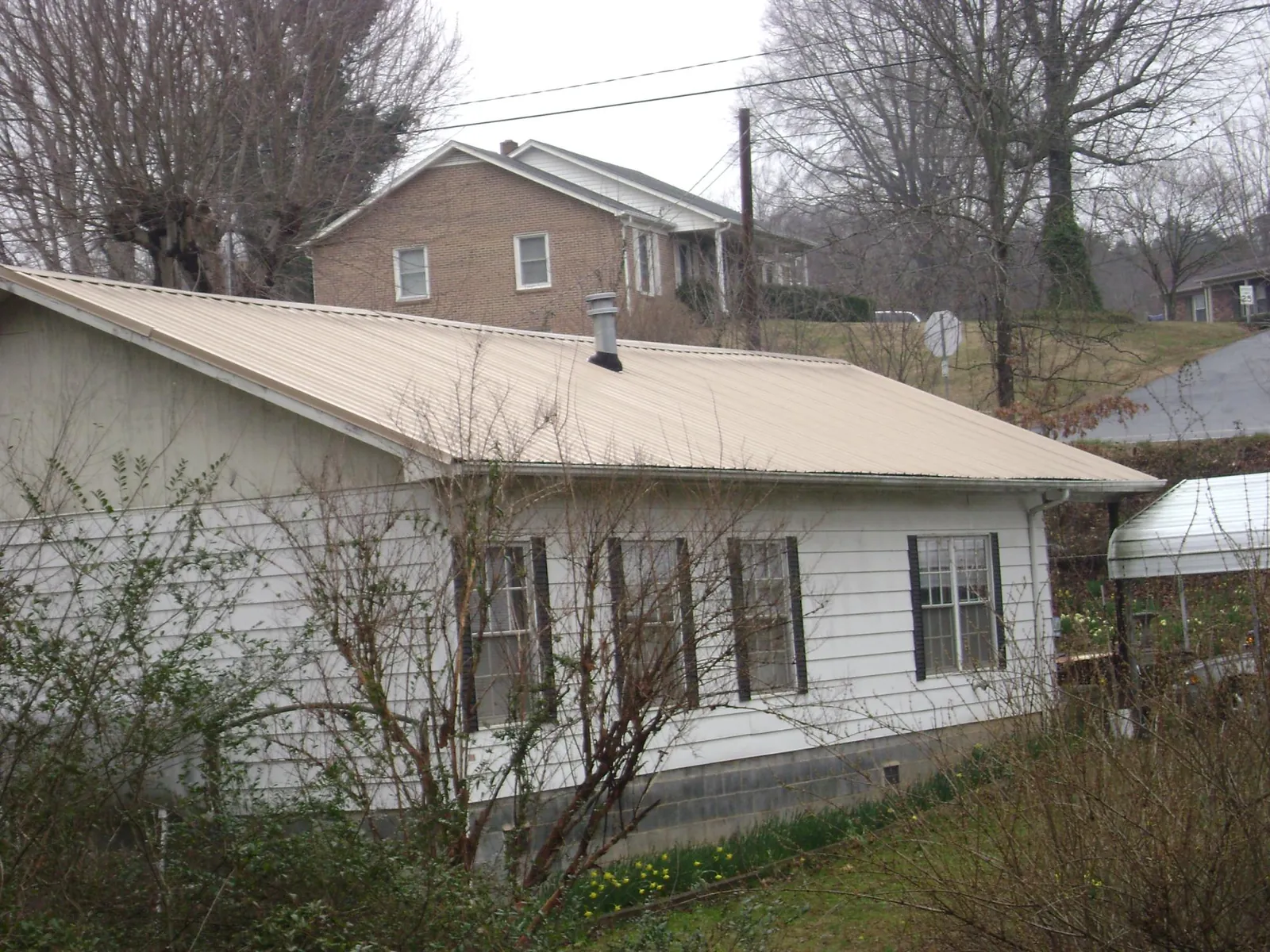 Tan metal roof on a white sided house set into a hillside — Commercial Roofing by Roofing Brothers in Century