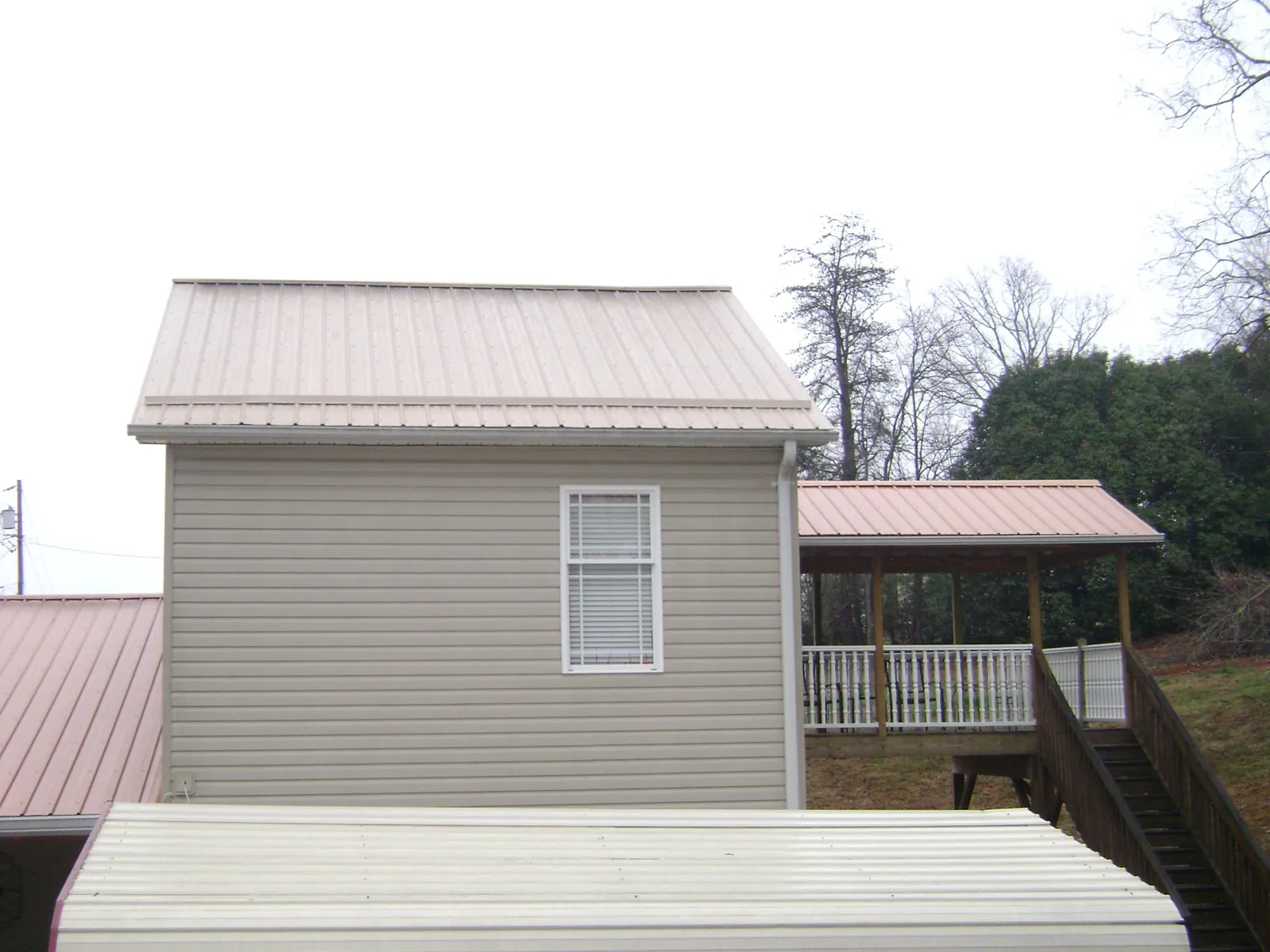 Tan metal roofs on a two story addition and attached porch, from a Roof Replacement job in Century